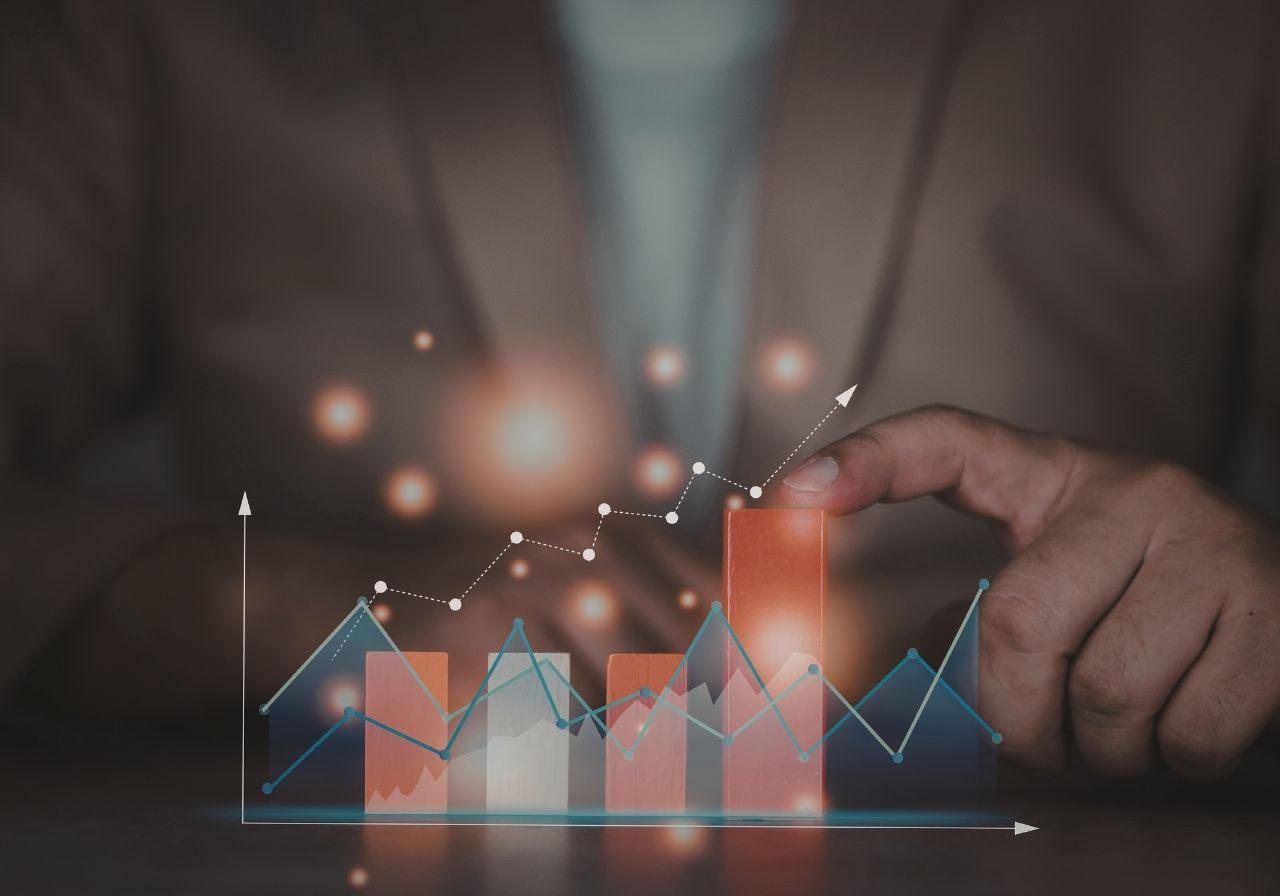 A person pointing at a digital bar graph with rising trends and data points, symbolizing financial growth and analysis.