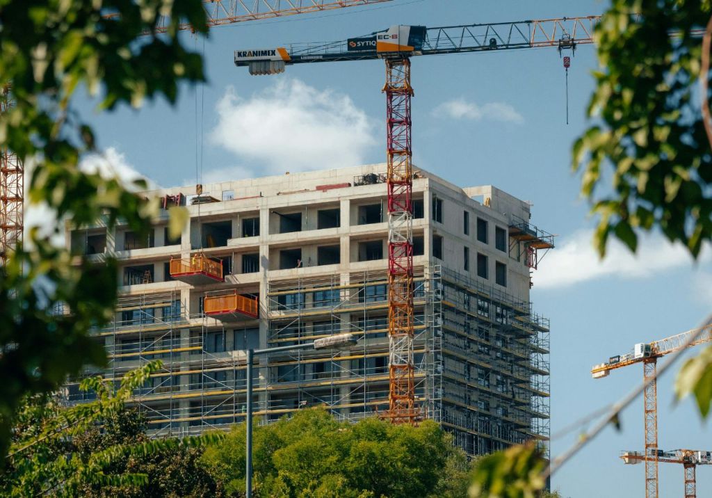 Construction site of a building with cranes and scaffolding against a blue sky.