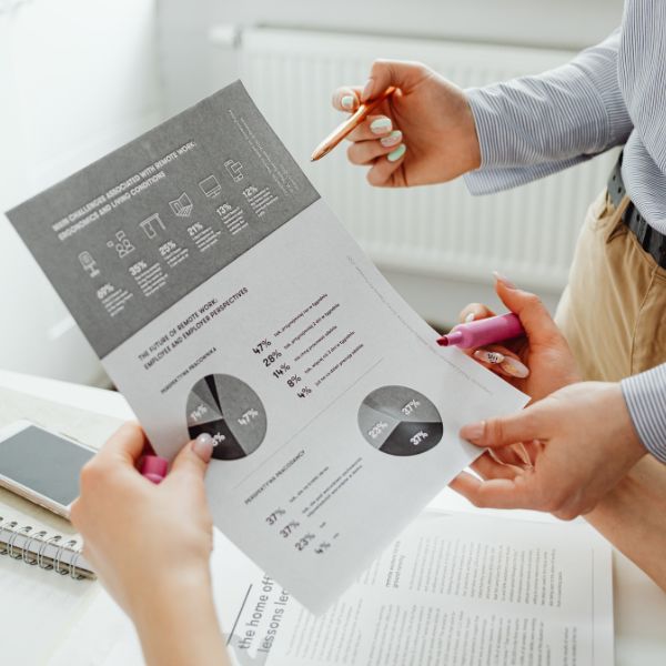 Two people discussing a printed document with graphs and statistics about remote work challenges and employee perspectives, with one person holding a pen and the other a highlighter.