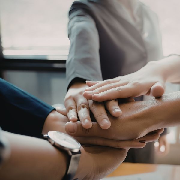 A group of hands from different individuals stacking on top of each other, symbolizing teamwork and collaboration in a business setting.