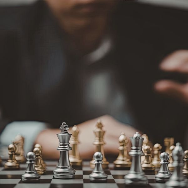 A person in a suit contemplating a chess move, with silver and gold chess pieces on a board.
