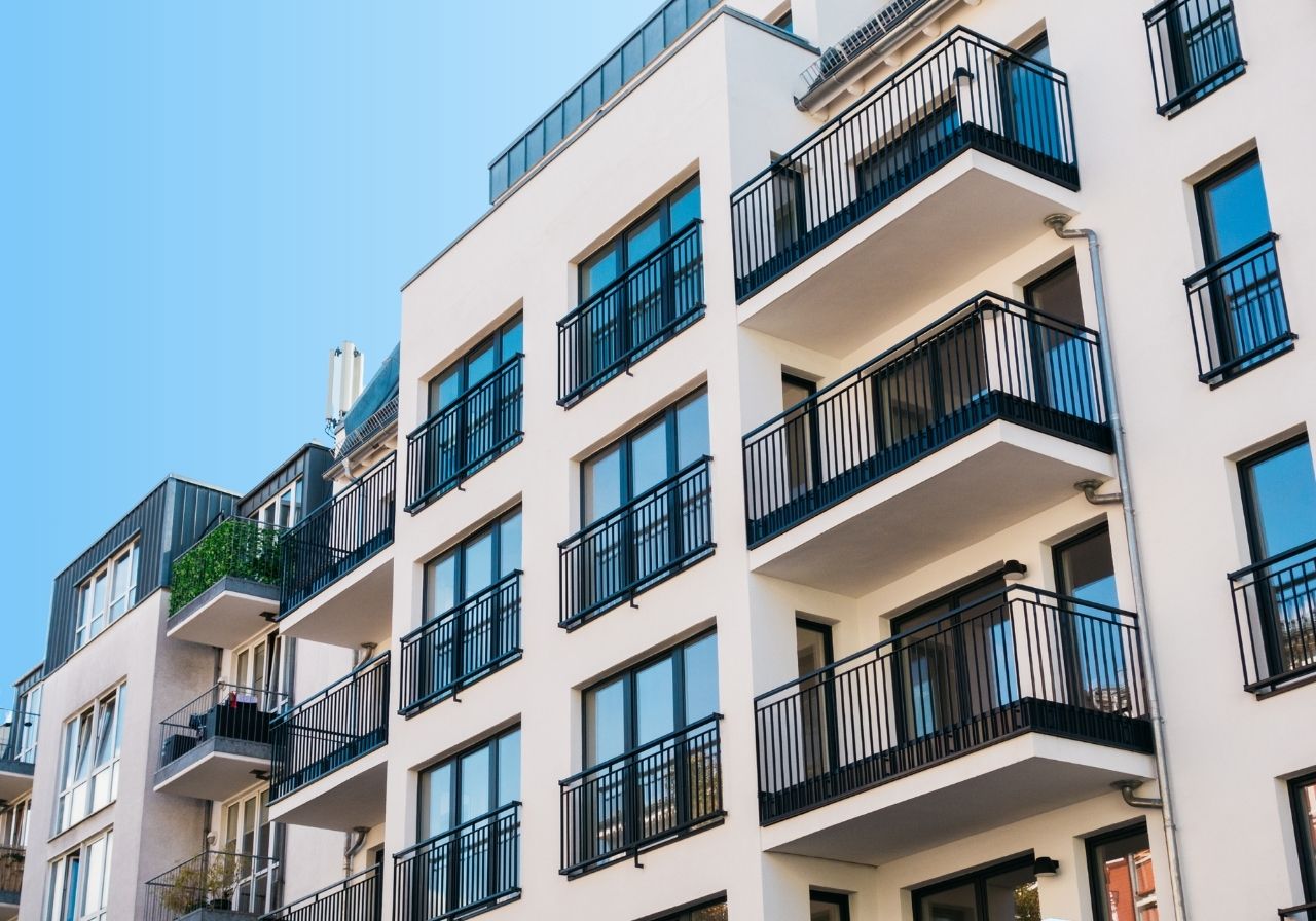 Modern apartment building with multiple balconies and large windows, against a clear blue sky.