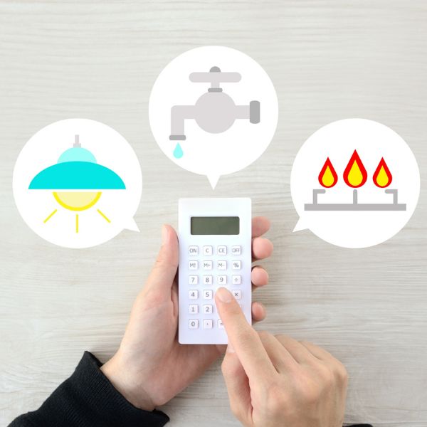 A person holding a calculator with icons of a light bulb, a faucet, and a gas stove above it, symbolizing utilities management.